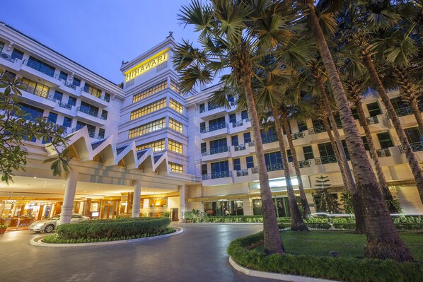 A multi-story hotel with a prominent 'HIMAWARI' sign, featuring a modern architectural design with balconies and a well-maintained garden with palm trees.