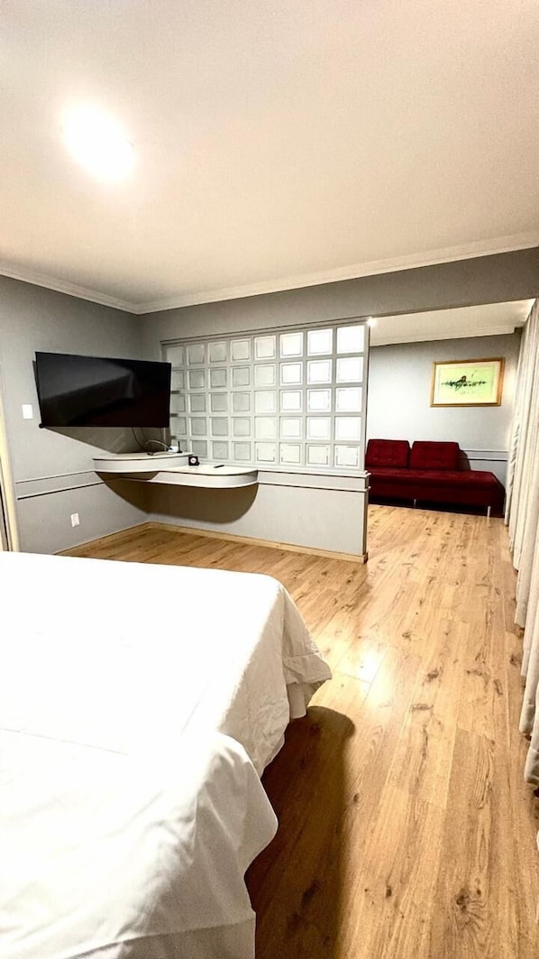 Quarto com cama, televisão na parede, janela com vista e sofá vermelho.