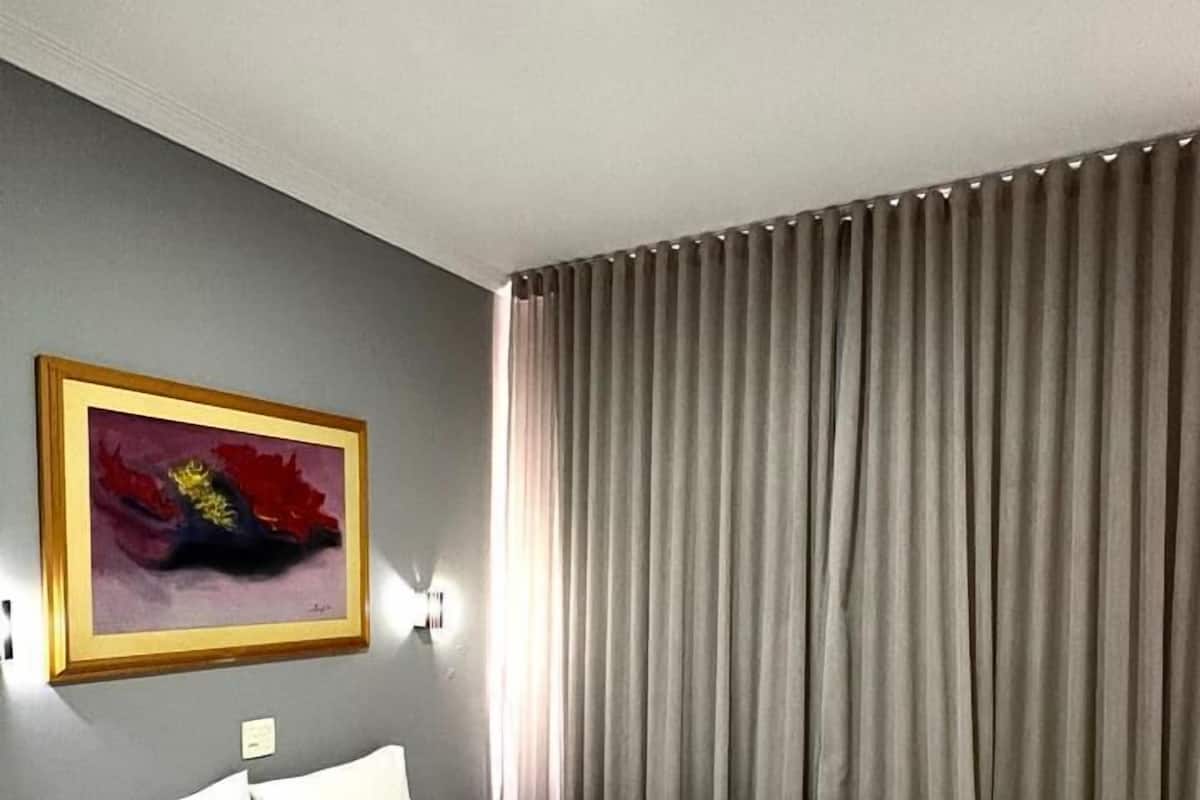 Une chambre d’hôtel avec un lit, un tableau au mur et une fenêtre avec des rideaux.