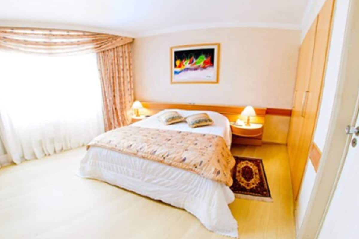 Une chambre d’hôtel avec un lit, une table de chevet, une lampe, un tableau au mur et une porte.