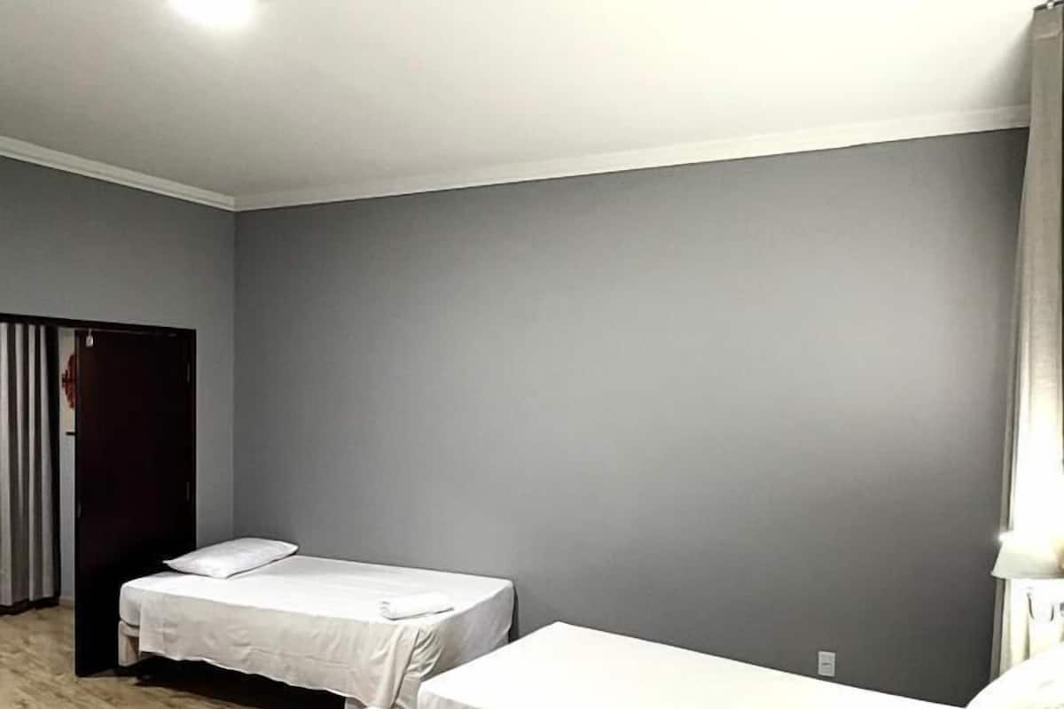 Une chambre avec deux lits simples, un plancher en bois, un mur gris et une porte.