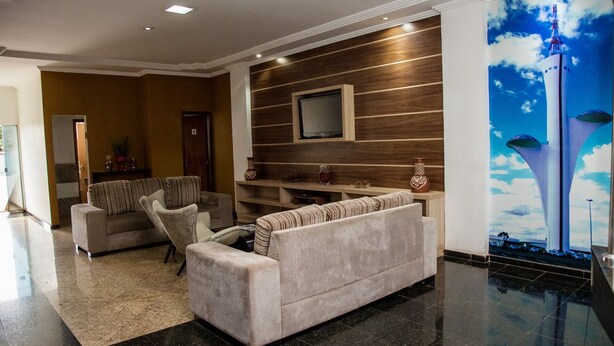 A modern lobby with a sofa, armchairs, a flat-screen TV mounted on a wooden wall, and a large mural of a cityscape.