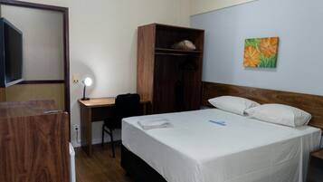 A hotel room with a bed, a desk, a wardrobe, and a painting on the wall.