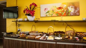 A buffet counter with various food items, a vase of red flowers, and a painting of flowers on the wall.