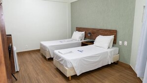 A hotel room with two single beds, a wooden headboard, a bedside table with a lamp, and a wooden floor.