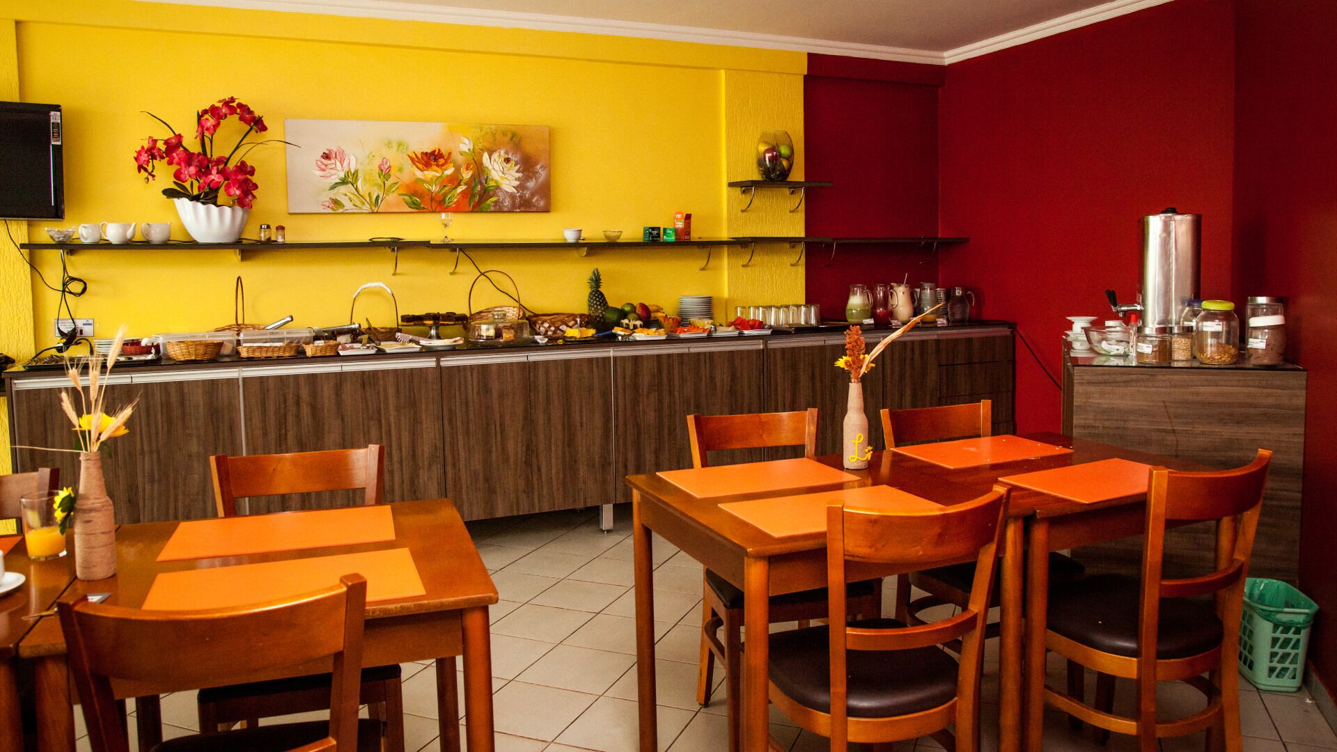 Un restaurant avec un mur jaune, des tables et des chaises en bois, et un mur d’accent rouge.