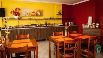 Un restaurant avec un mur jaune, des tables et des chaises en bois, et un mur d’accent rouge.