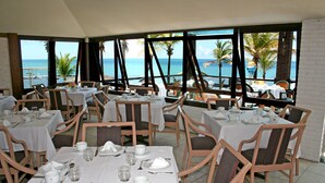 Ein Restaurant mit gedeckten Tischen mit Blick auf einen Strand mit Palmen und den Ozean.