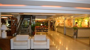 Eine Hotelhalle mit Empfangstresen, zwei Sofas, einer Treppe und einem Essbereich.