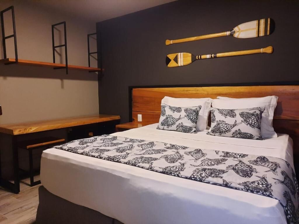 Un dormitorio con cama, almohadas, cabecera de madera, un banco y dos palas en la pared.