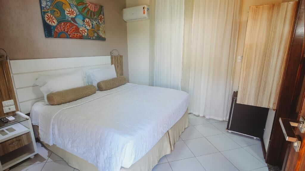A hotel room with a bed, a bedside table, a wall-mounted air conditioner, and a curtain.