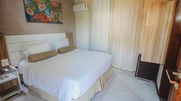 A hotel room with a bed, a bedside table, a wall-mounted air conditioner, and a curtain.