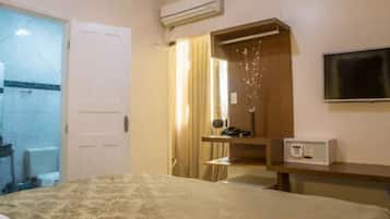 Quarto de hotel com cama, secretária, ar condicionado, televisão e casa de banho visível através de uma porta aberta.