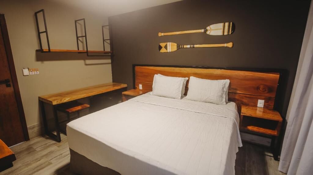 Un dormitorio con una cama de madera, dos mesitas de noche, un banco de madera y dos tablas de remo en la pared.