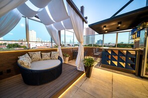 A rooftop terrace with a circular seating area, a potted plant, and a view of the city skyline. - Hotel Meridional (Fortaleza)