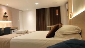 Une chambre d’hôtel avec un lit, un bureau et une chaise. Il y a une fenêtre avec des rideaux.