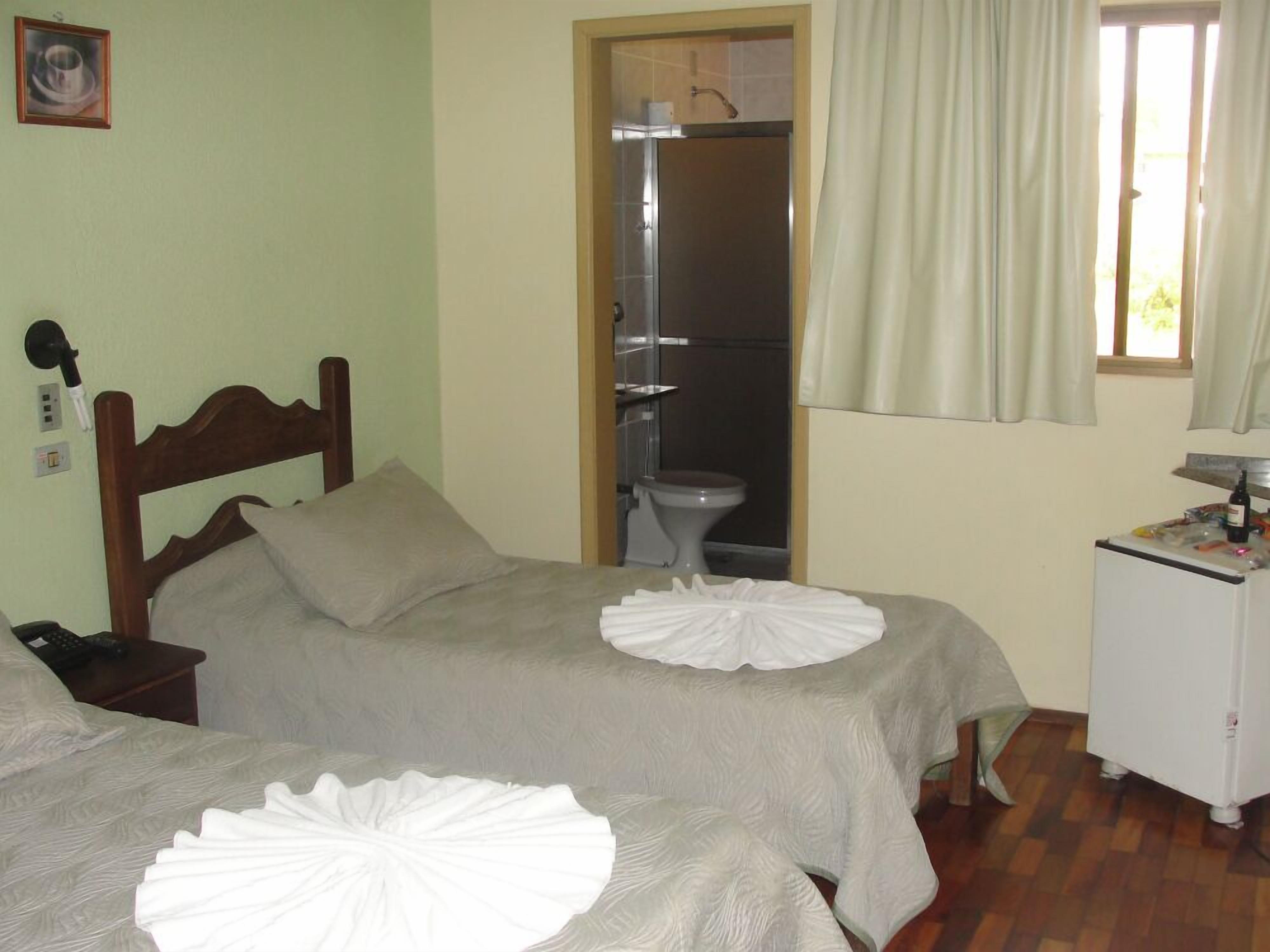A room with two beds, a small bedside table, a nightstand, a white cabinet, and a bathroom door.