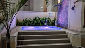 Une piscine avec de l’eau qui dévale en cascade sur des marches, entourée de plantes vertes et d’un mur de briques.