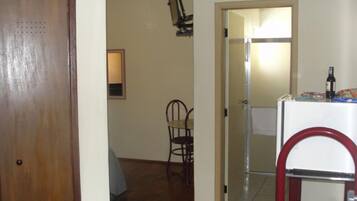 Una habitación con puerta de madera, una pequeña mesa con una silla, una pared blanca y una puerta que da a otra habitación.