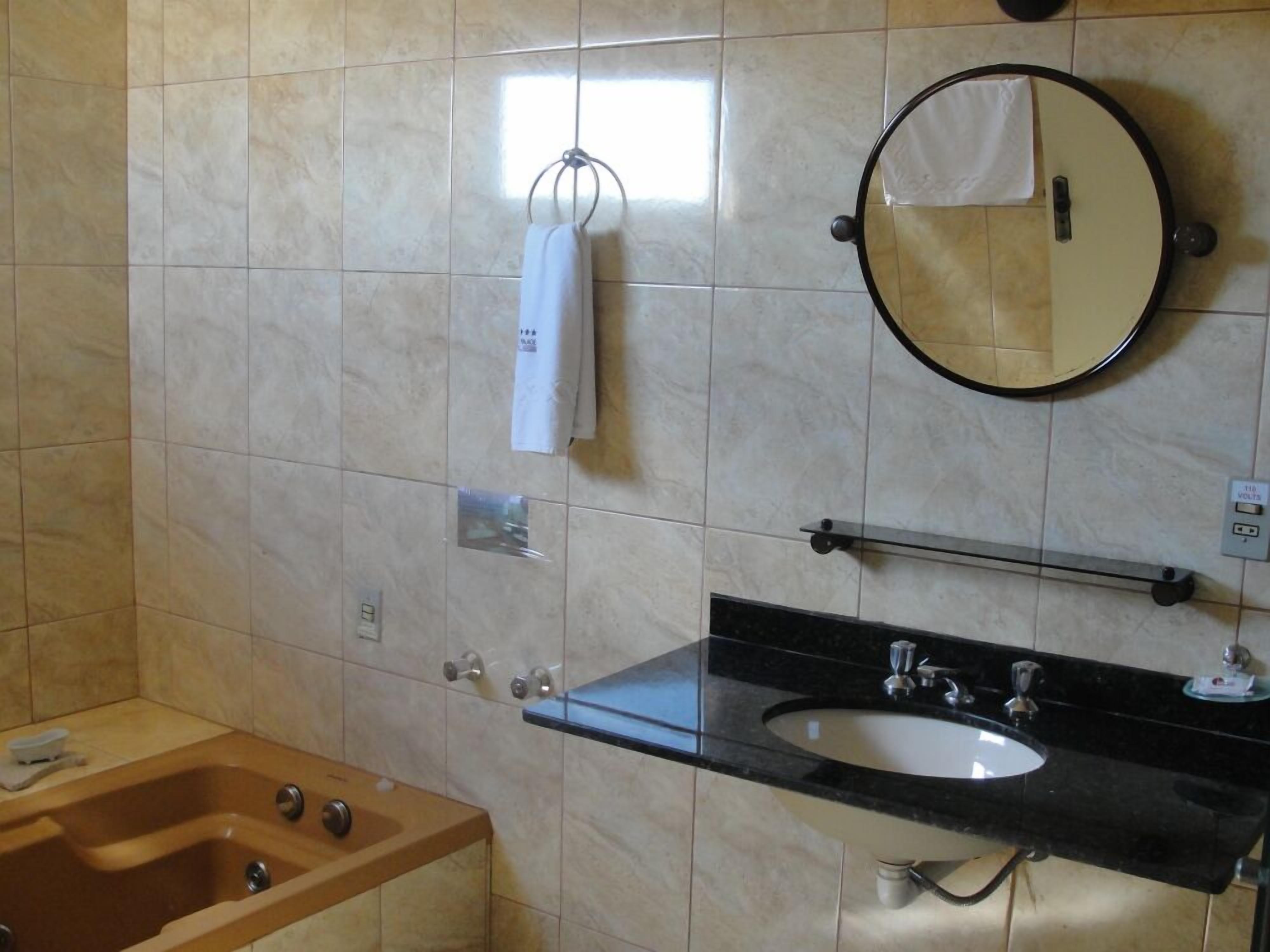 A bathroom with a wooden bathtub, a black sink with a mirror above it, and a towel hanging on a rack.