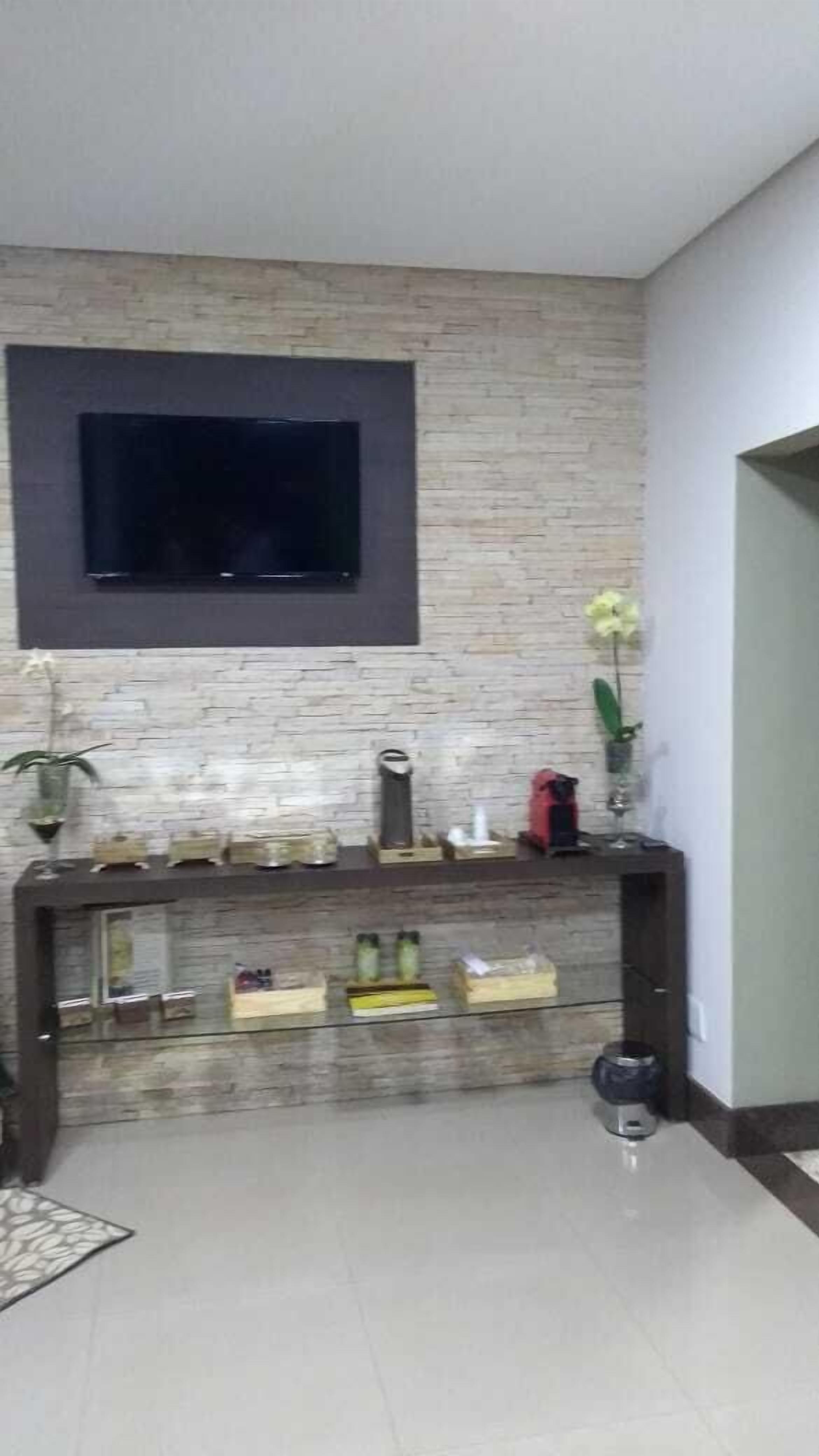 Een kamer met een wandgemonteerde flatscreen televisie, een console tafel met diverse voorwerpen en een betegelde vloer.