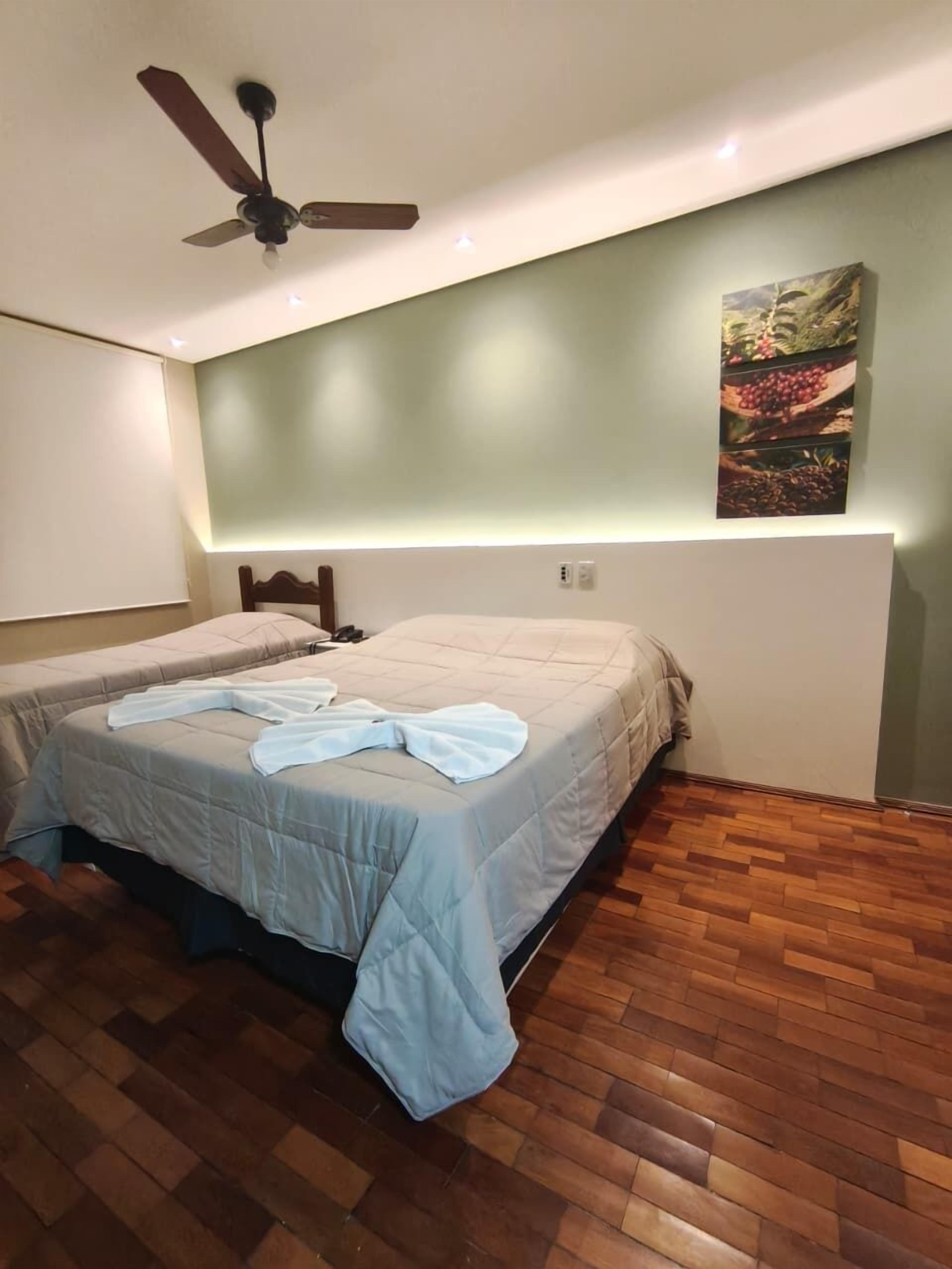 Een kamer met twee bedden, een plafondventilator, houten vloeren en een kunstwerk aan de muur.