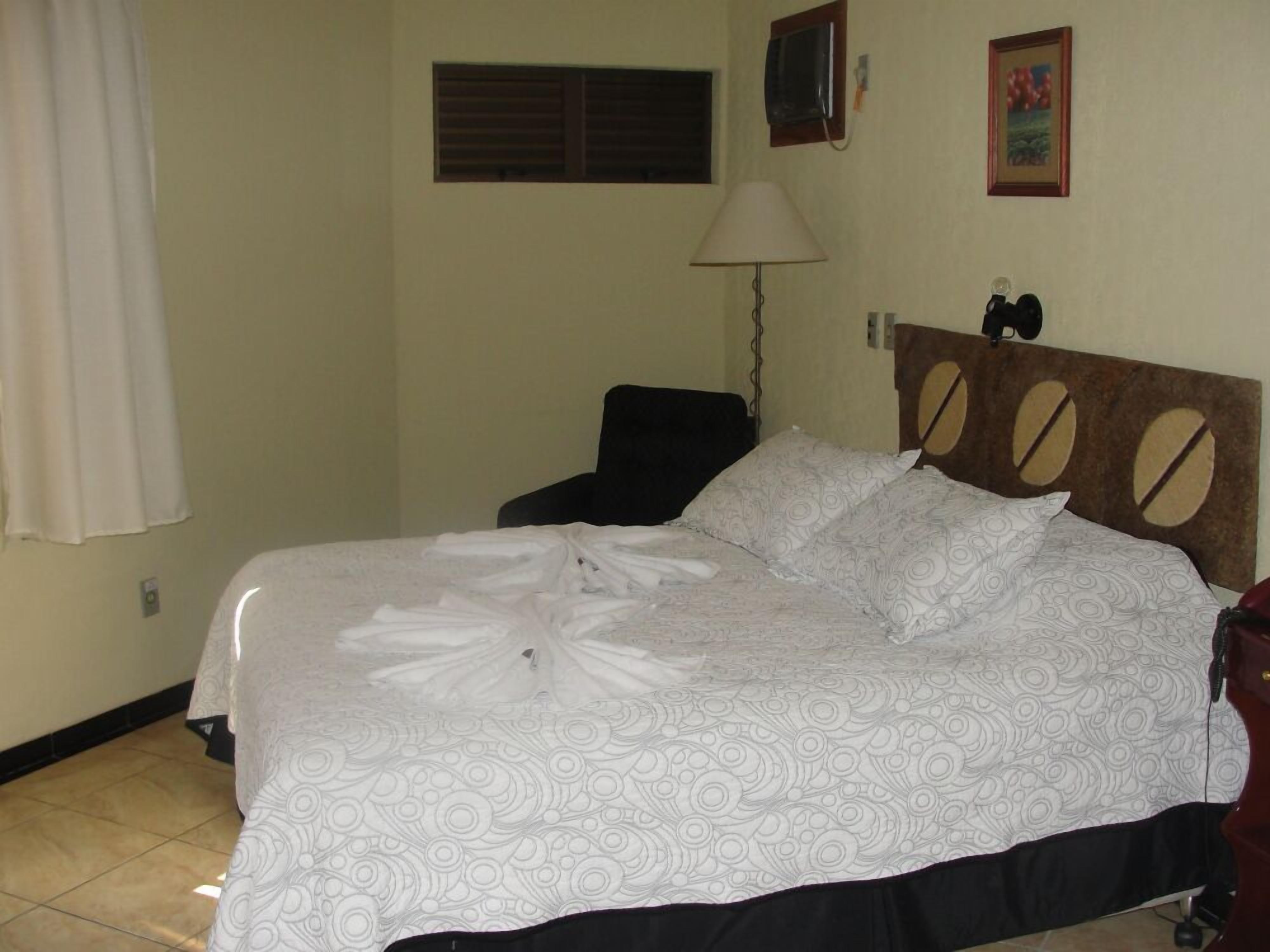 A neatly made bed with a patterned bedspread, a bedside lamp, and a chair in a room with a simple decor.