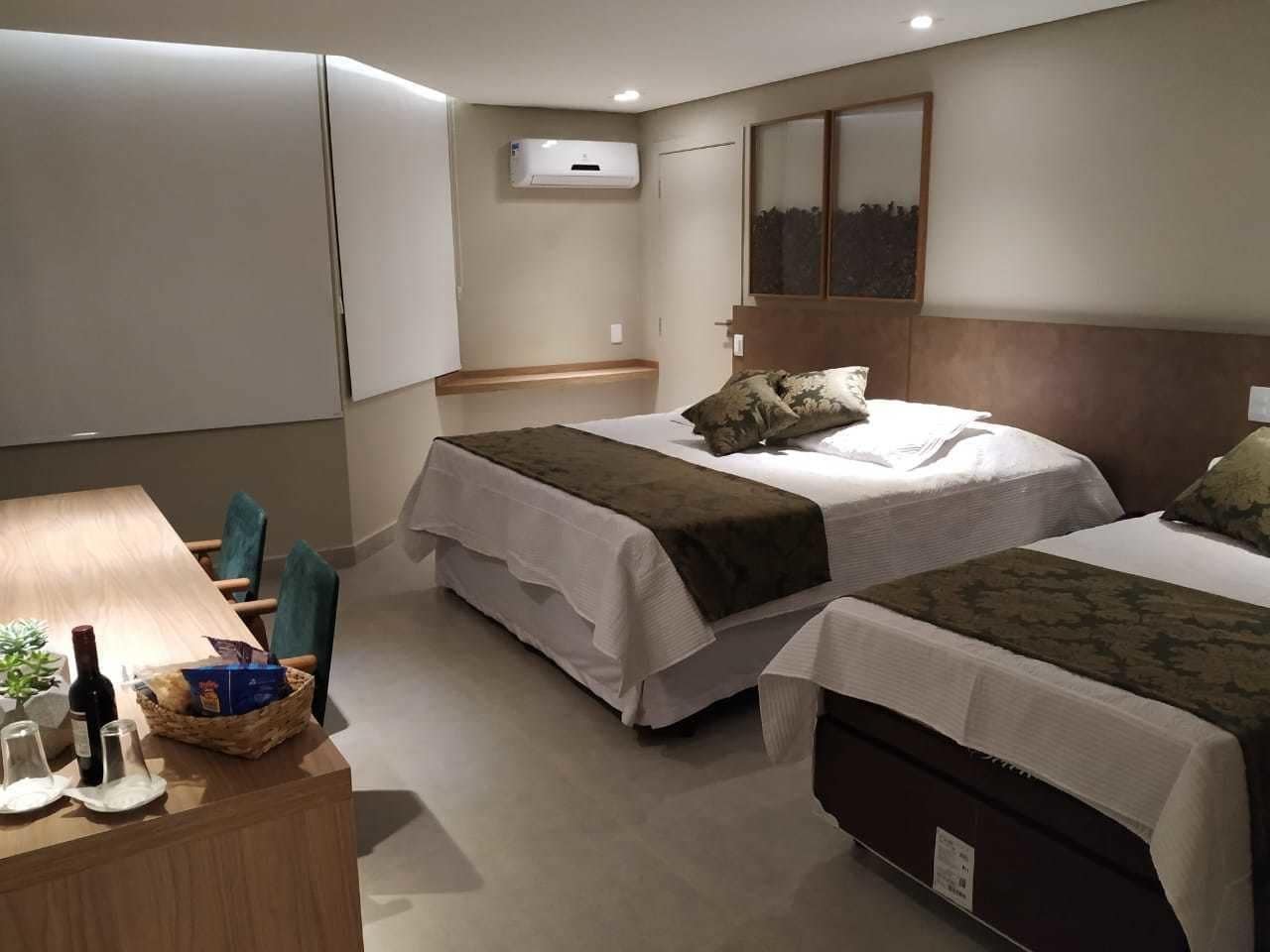 Habitación de hotel con dos camas, un escritorio de madera, una planta pequeña y un aire acondicionado instalado en la pared.