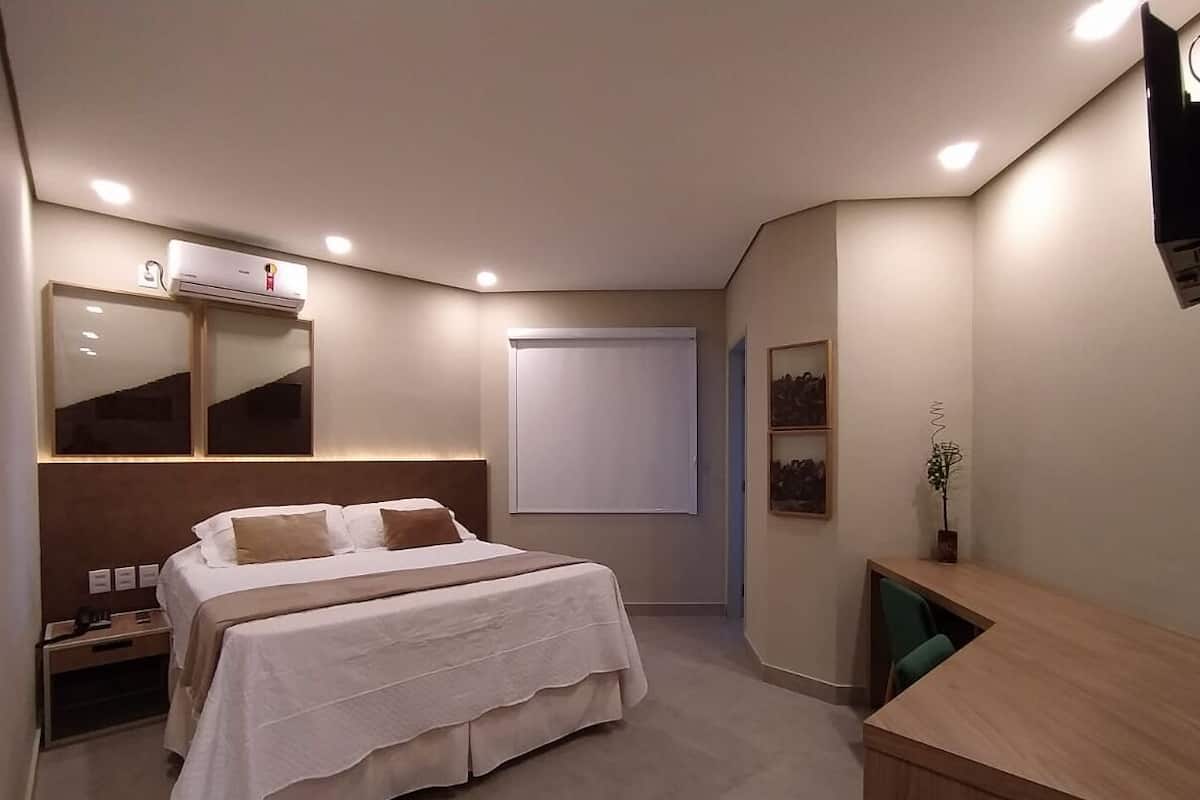 Ein Schlafzimmer mit Bett, Nachttischen, einem Schreibtisch, einem Spiegel und einer Klimaanlage.