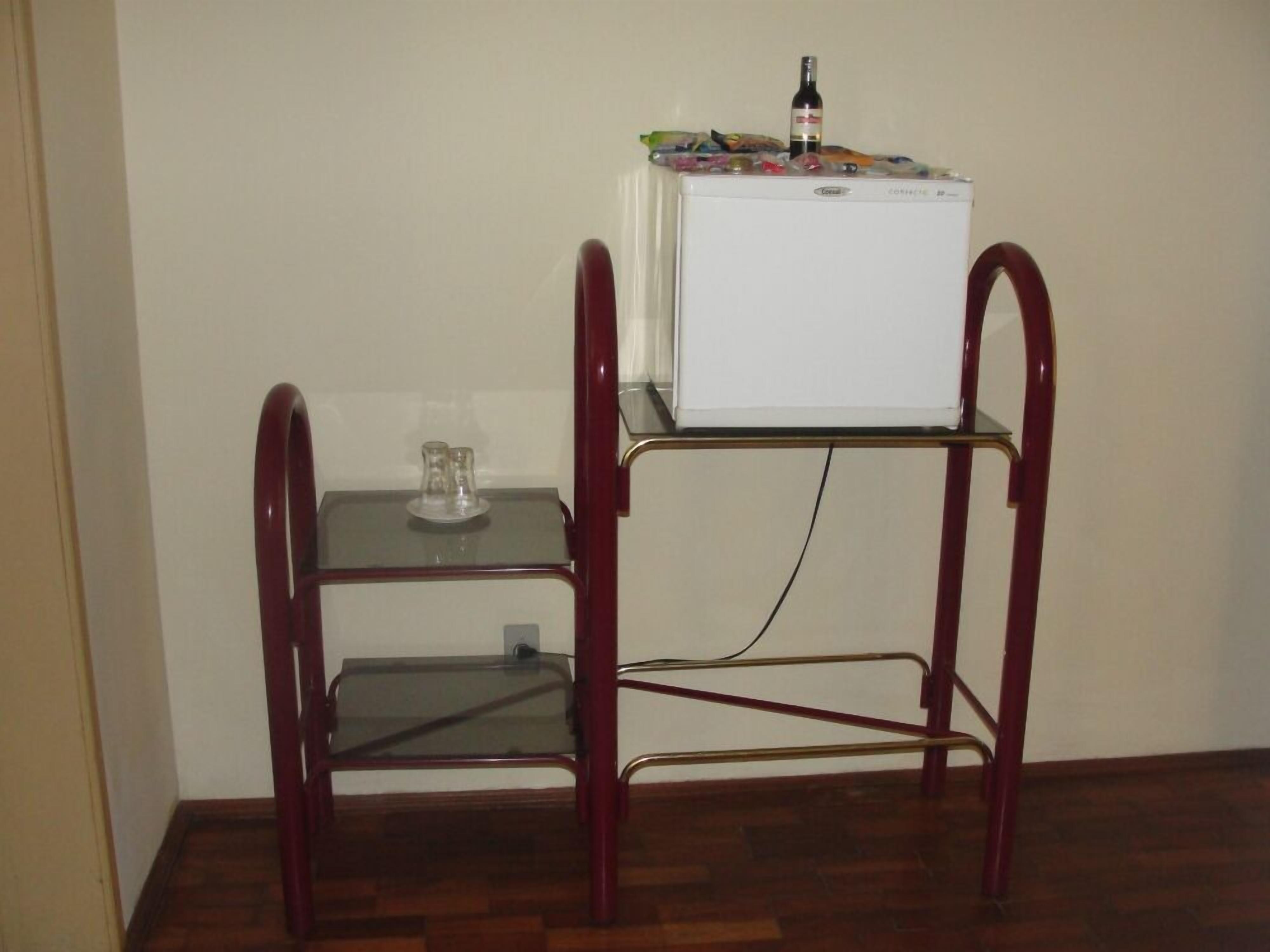 Una pequeña cocina americana con un refrigerador blanco, una mesa de vidrio y una silla.