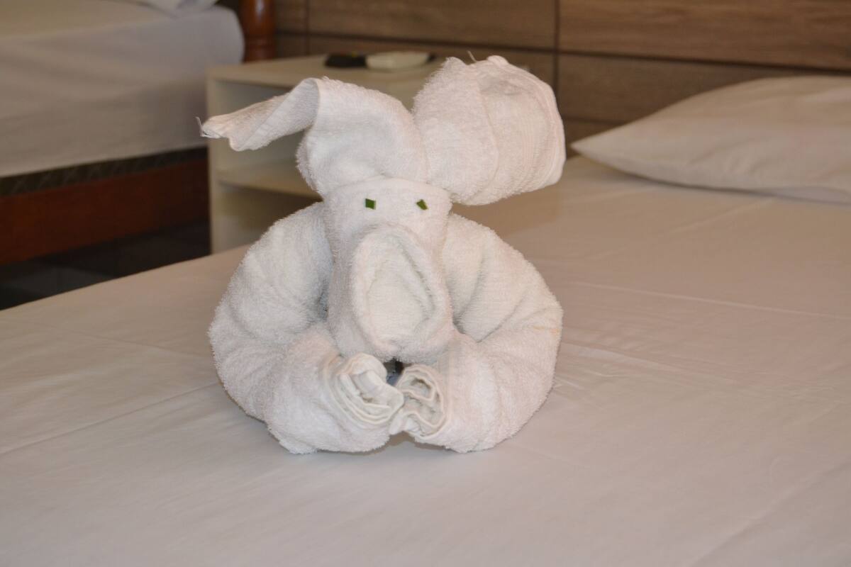Un elefante hecho con una toalla, ordenado, sobre una cama en una habitación de hotel.