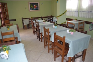 A dining area with multiple tables and chairs, each with a tablecloth and potted plants. - Pousada Porto Tropical (Ipojuca)