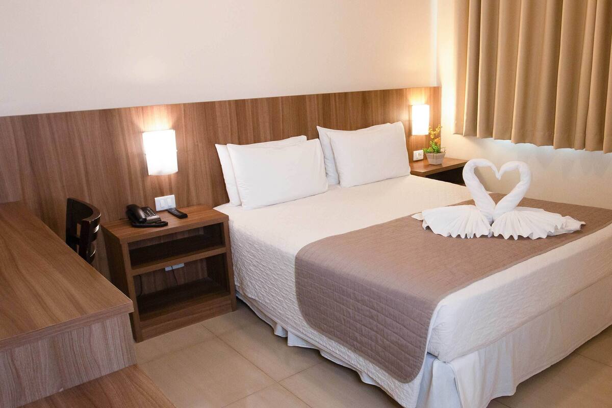 Ein Hotelzimmer mit einem ordentlich bezogenen Bett, einem Nachttisch mit Telefon und einer Wandlampe.