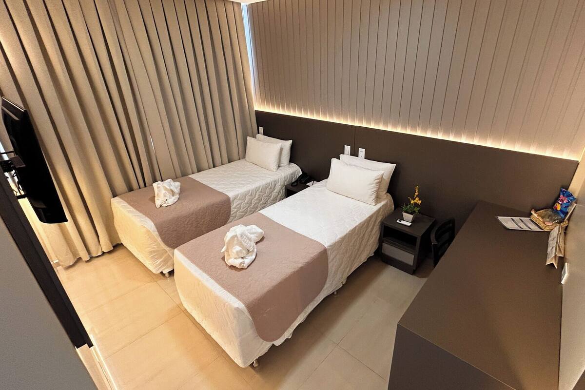 Ein Hotelzimmer mit zwei Betten, einem Nachttisch mit Lampe, einer kleinen Pflanze und einem Fernseher.