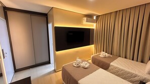 Ein Hotelzimmer mit zwei Betten, einem an der Wand montierten Fernseher und einem Vorhang.