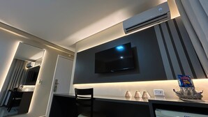 Ein Hotelzimmer mit einem Wand-Fernseher, einem Schreibtisch mit Stuhl und einer Klimaanlage.