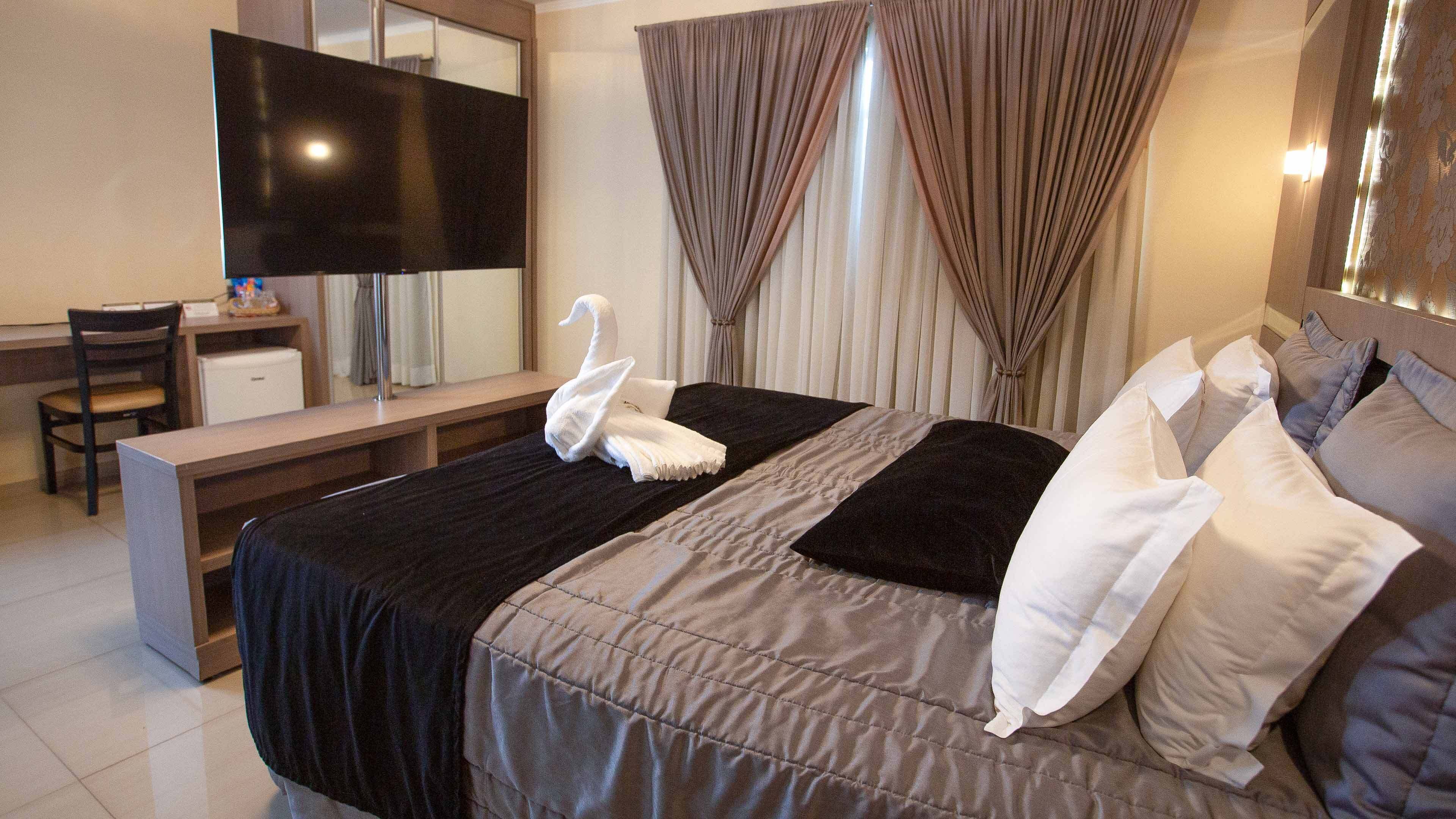 A hotel room with a bed, a desk with a flat-screen TV, a chair, and curtains.