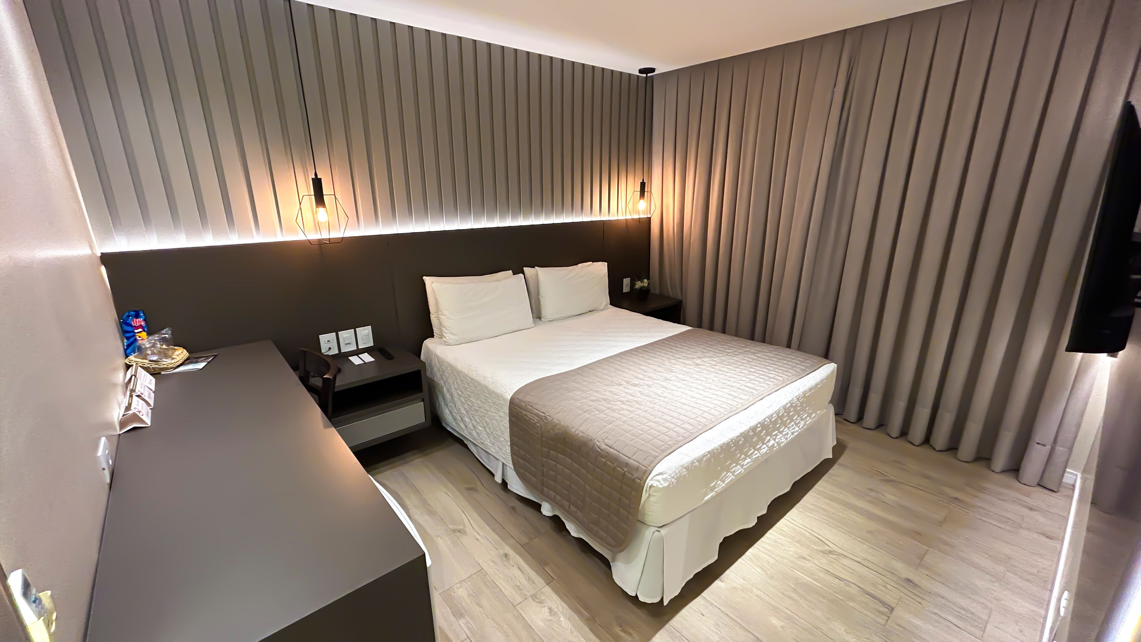 Une chambre d’hôtel comprenant un lit, des tables de chevet, un bureau et un luminaire fixé au mur.