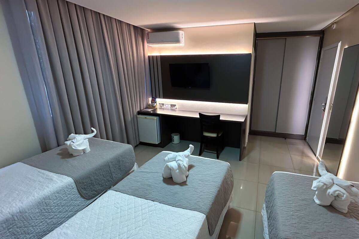Ein Hotelzimmer mit drei Betten, einem Schreibtisch, einem Flachbildfernseher und einem Spiegel.