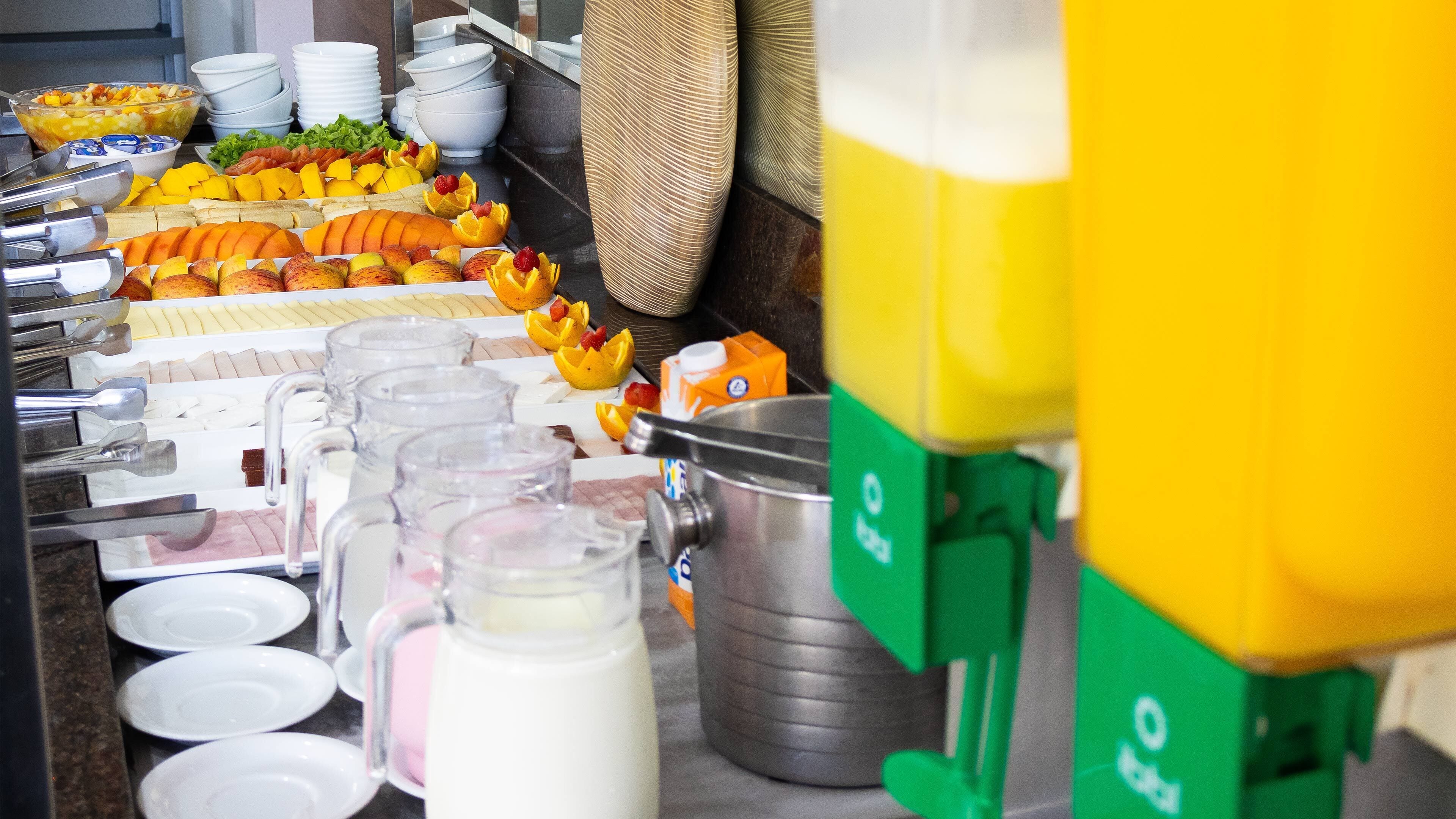 A buffet with various fruits, beverages, and a milk jug.