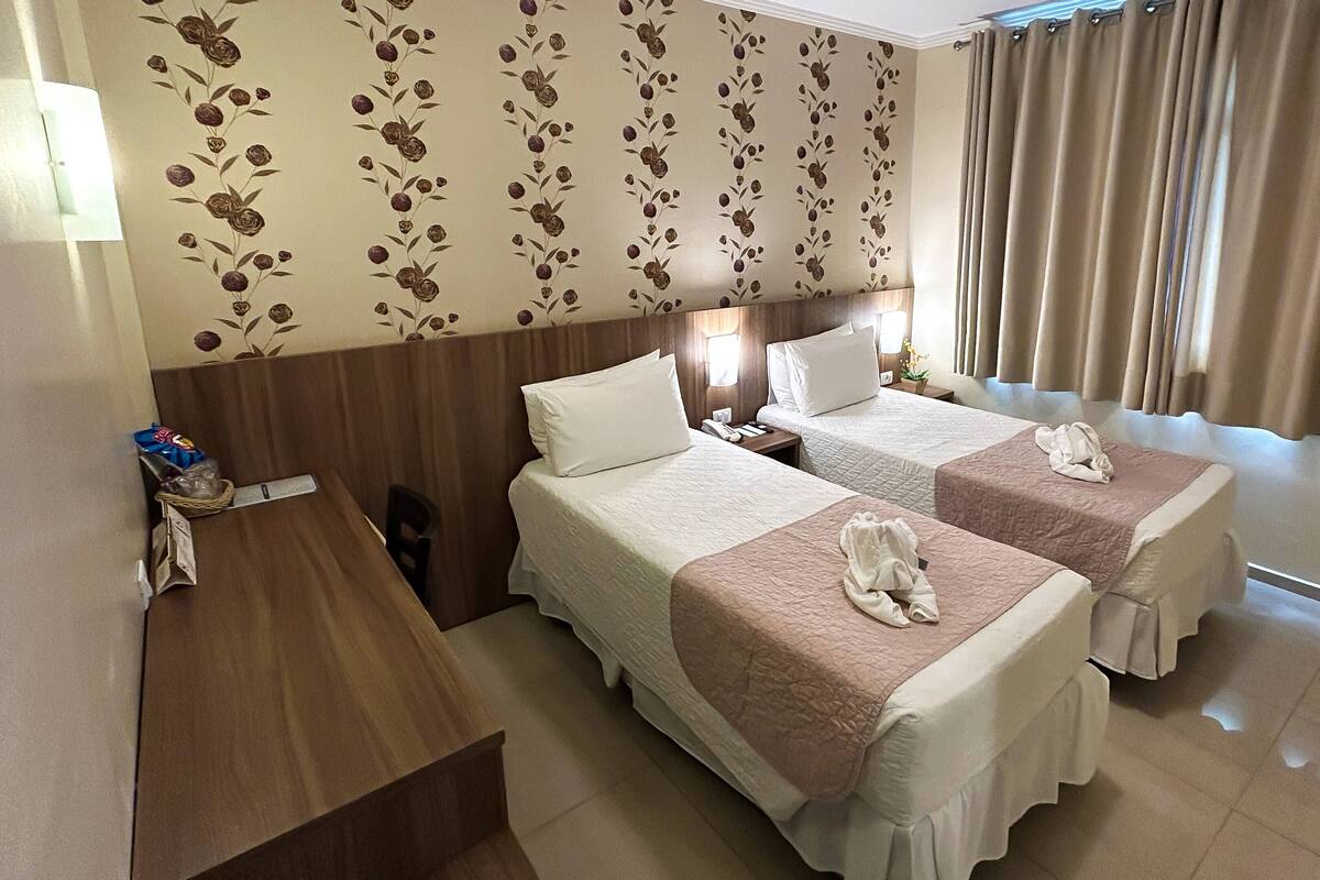 Ein Hotelzimmer mit zwei Betten, einem Holztisch, einem Telefon und einer Wand mit floralem Wandpapier.