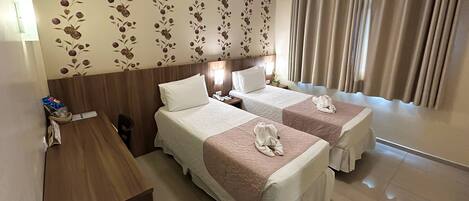 Habitación de hotel con dos camas, un escritorio de madera, un teléfono y una pared con papel tapiz floral.