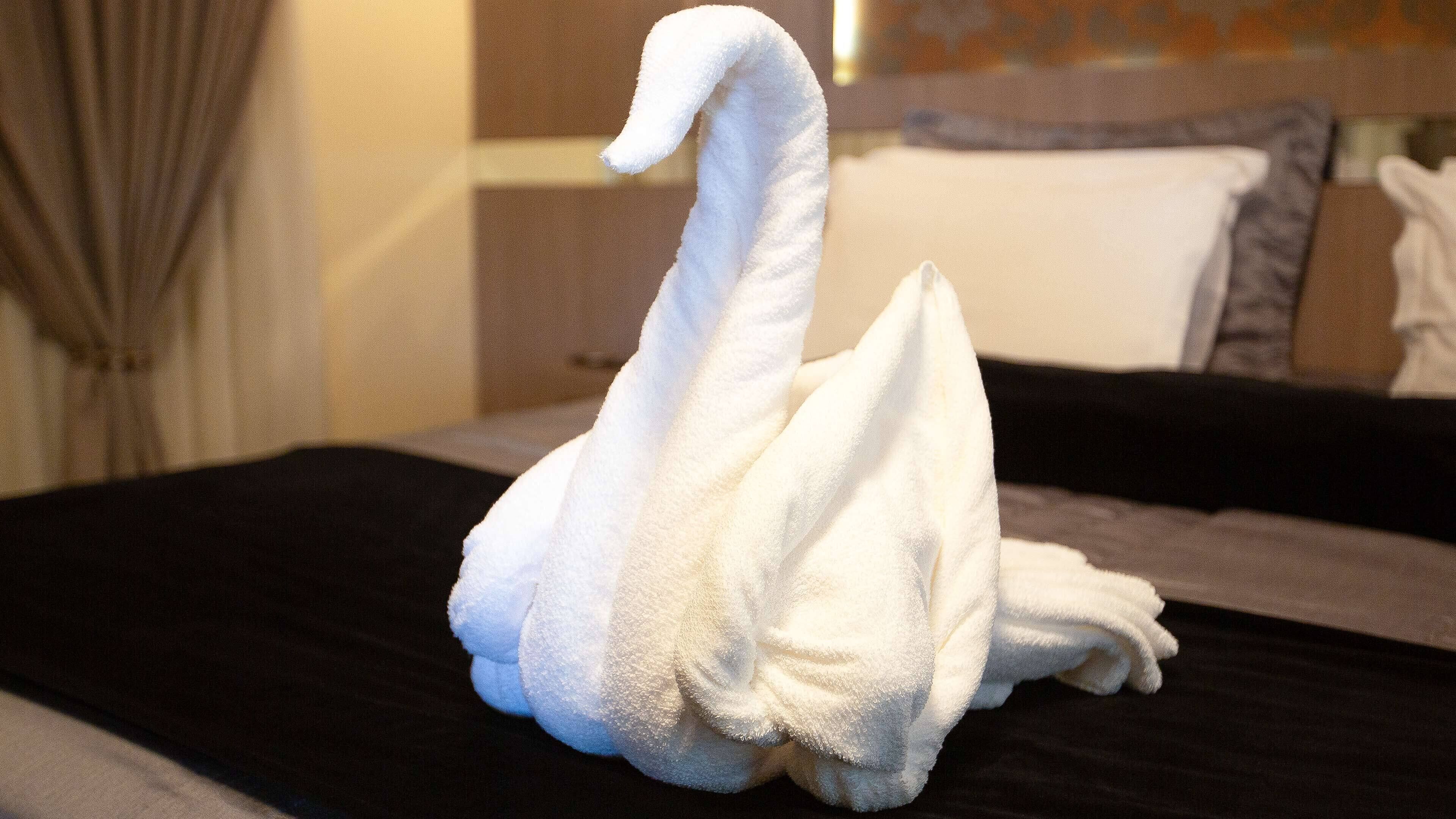 Une serviette en forme de cygne est posée sur un lit dans une chambre d’hôtel.