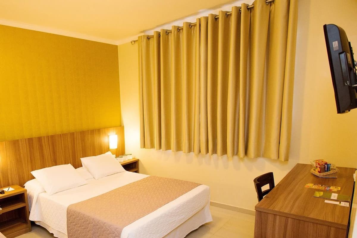 Ein Hotelzimmer mit Bett, Nachttischen, Schreibtisch und Fernseher.