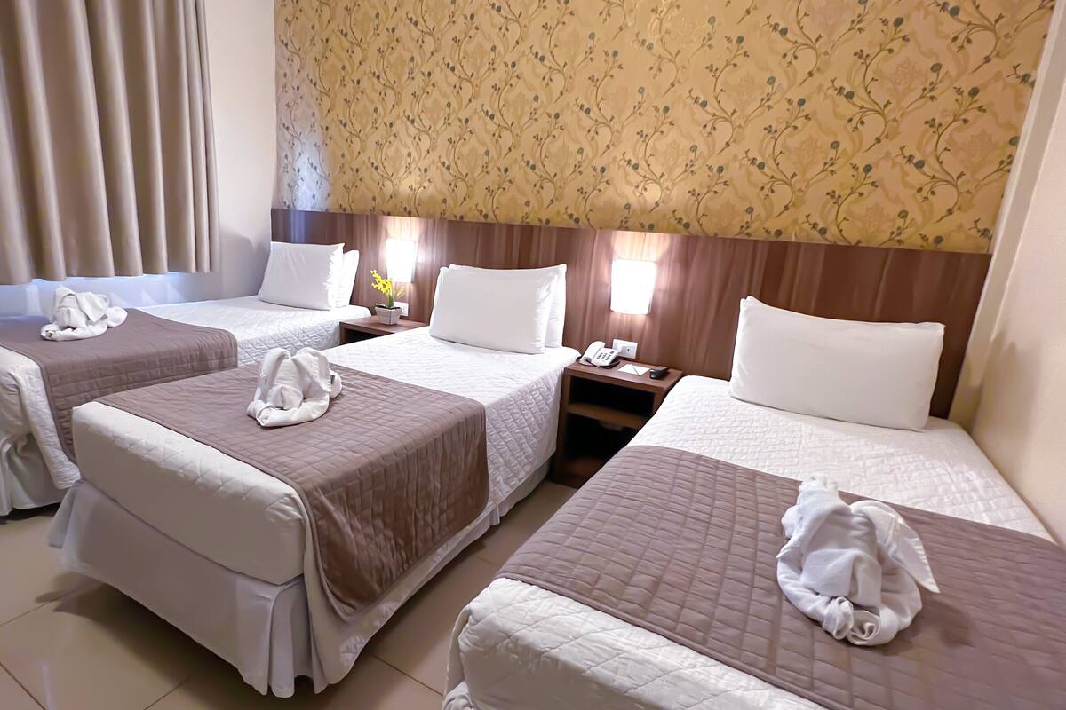Ein Hotelzimmer mit zwei Betten, jedes mit einem Kopfkissen und einem Handtuch. Ein Nachttisch mit Telefon und Lampe ist vorhanden.