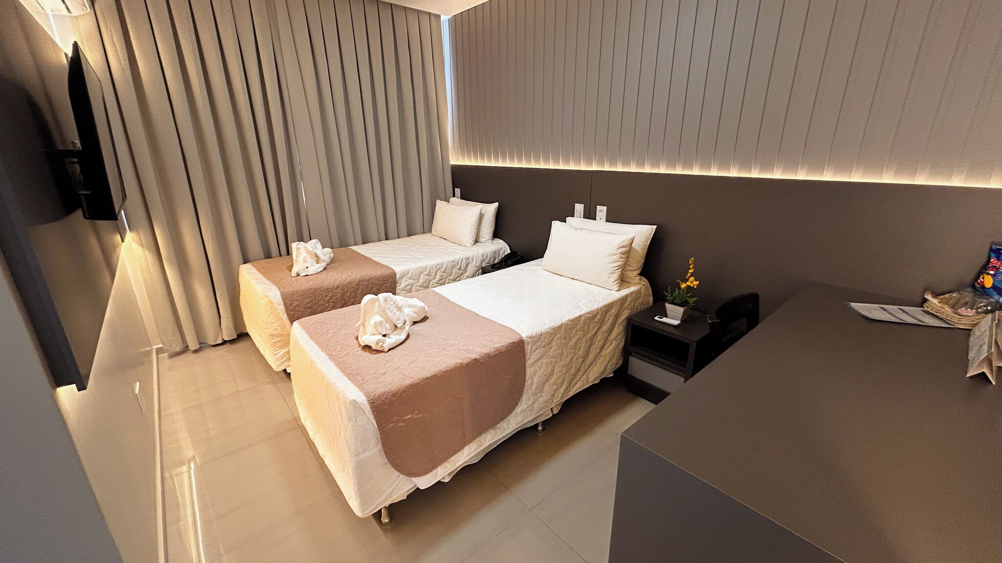 Een hotelkamer met twee bedden, een bureau, een stoel, een nachtkastje en een televisie.