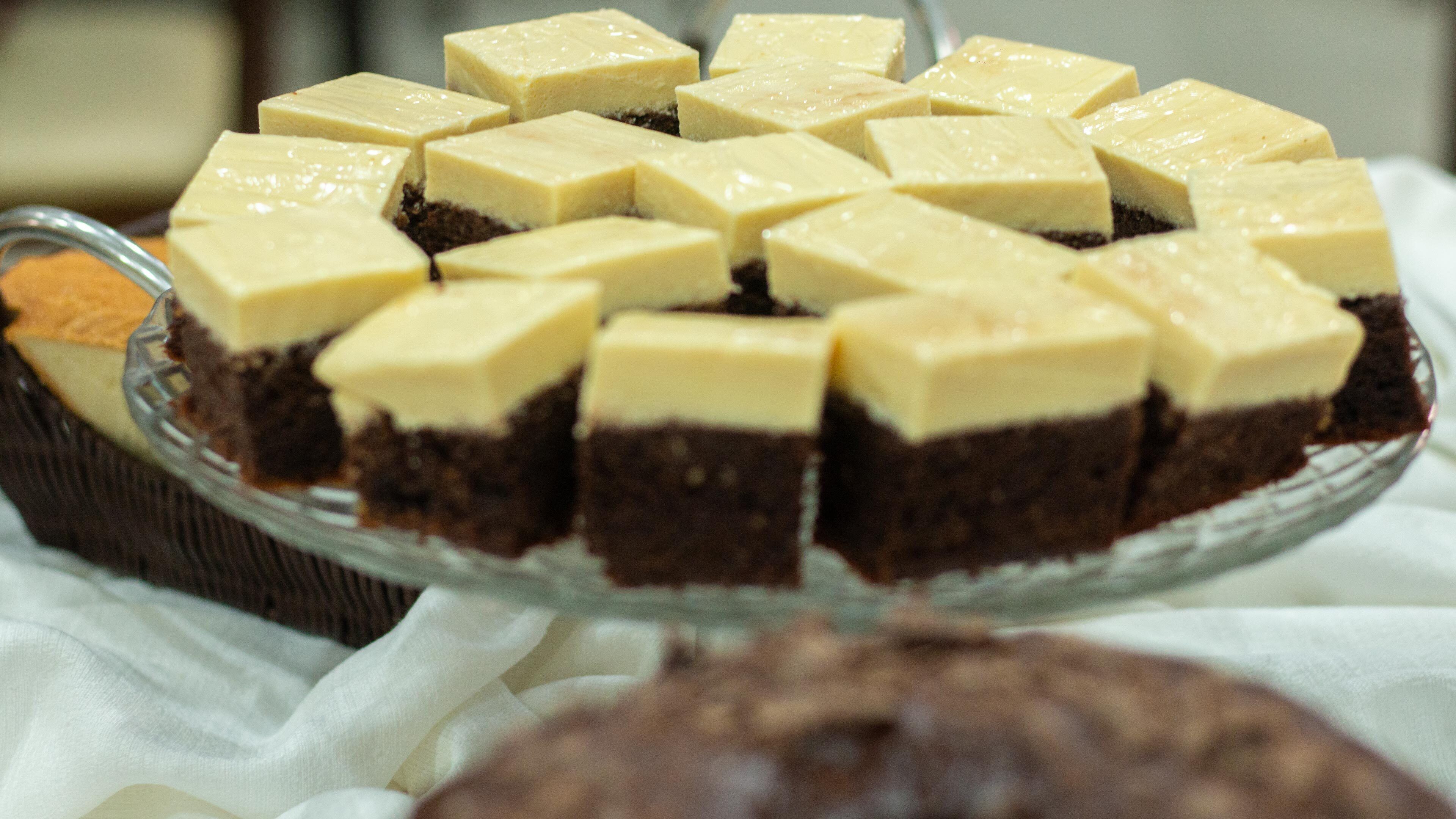 A glass serving tray with several square pieces of cheesecake and a slice of cake with a crumbly base.