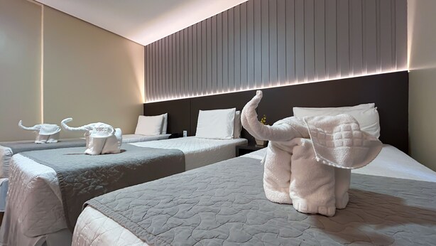 Ein Hotelzimmer mit zwei Betten, einem Kopfteil mit vertikalen Lamellen und zwei elefantenförmigen Handtüchern auf den Betten.