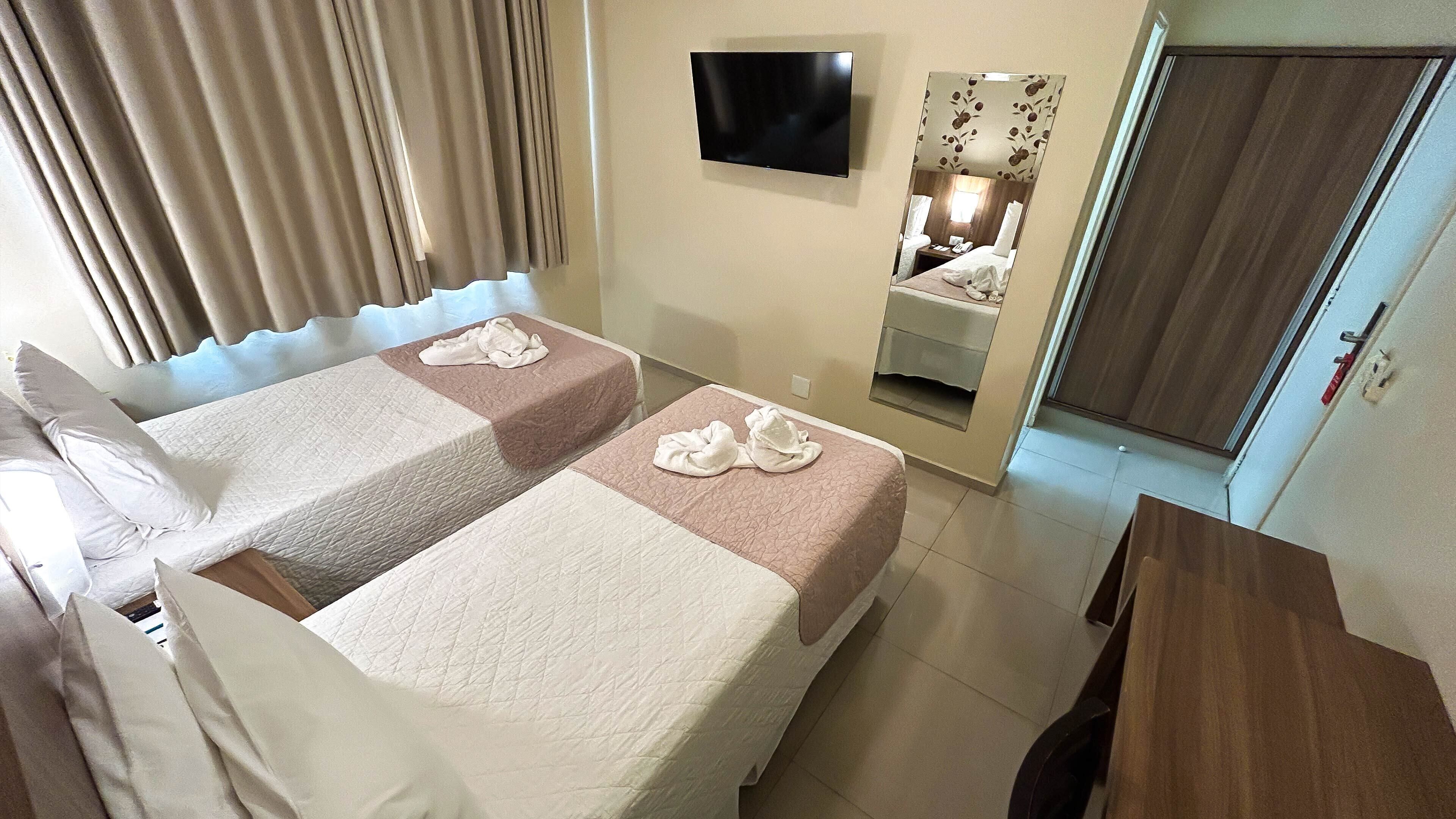 Ein Hotelzimmer mit zwei Betten, einem an der Wand montierten Fernseher, einem Spiegel und einer Tür.