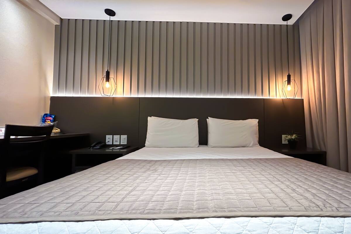Ein Hotelzimmer mit einem großen Bett, zwei Nachttischen, einem Schreibtisch mit Stuhl und einer Zimmerpflanze.